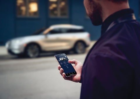 A person is shown interacting with a smartphone to connect to a Lincoln vehicle across the street. | Miller Lincoln in Saint Cloud MN