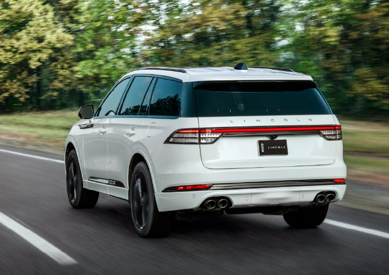 A white 2026 Lincoln Aviator® SUV is being driven away down a road lined with colorful trees. | Miller Lincoln in Saint Cloud MN
