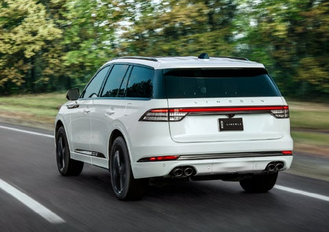A white 2026 Lincoln Aviator® SUV is being driven away down a road lined with colorful trees. | Miller Lincoln in Saint Cloud MN