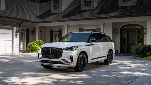 A white 2026 Lincoln Aviator® SUV is parked in the driveway of a luxury home. | Miller Lincoln in Saint Cloud MN
