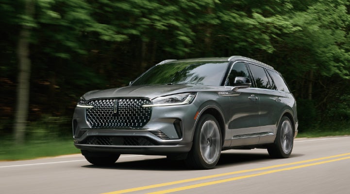 A 2027 Lincoln Aviator® SUV is being driven down a road lined with trees. | Miller Lincoln in Saint Cloud MN