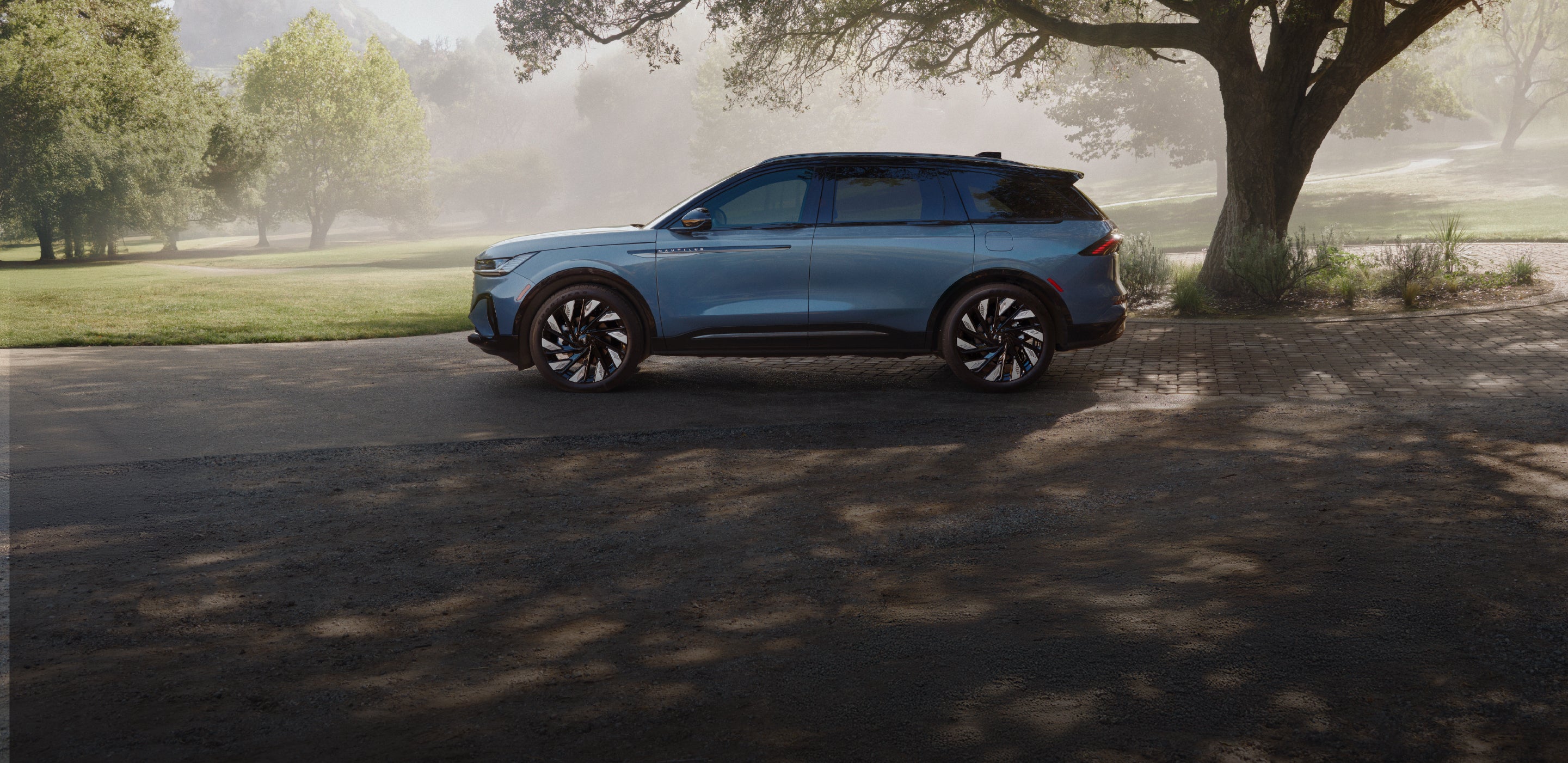 A 2026 Lincoln Nautilus® SUV parked beneath a large tree in a park landscape.